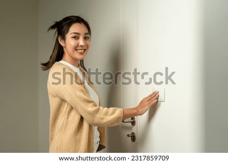 Earth Hour. Asian beautiful woman turn off or on the light to saving electrical energy. Finger pushing light switch turn on or off. White switch