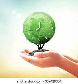 Earth Hour Concept: Human Hands Hold And Save Clock Time Of Earth Planet On Blurred Nature Background