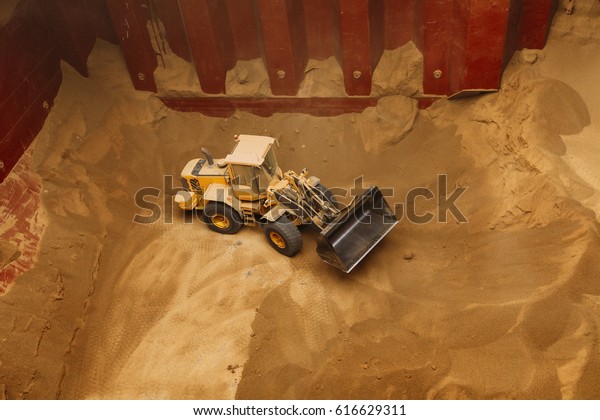 An earth mover arranging the gluten\
inside the pit of a grain freighter ship, for easier access for the\
machinery that is emptying the\
pit.