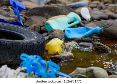 Earth Plastics Pollution Global Enviroment Emergency. Old Car Tire In Dirty Water Stream With Plastic Bottles And Trash.