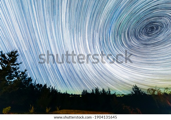The Earth rotation as seen in the night sky with\
the star trails. An awe scenery in the outdoors with the forest,\
the trees and the stars glowing in the distance. A dreamlike and\
colorful scenery