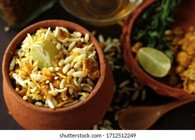 Earthen pot full of delicious Bengali traditional street food and evening snack, jhalmuri, is placed on a wooden base with its ingredients arranged in a earthen plate. The spoon is there for to serve.