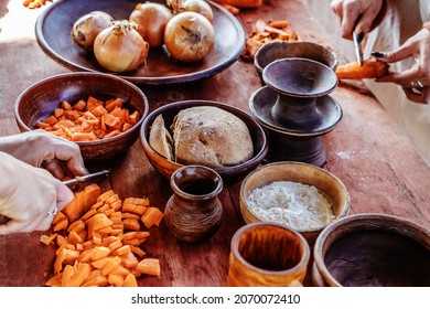 Earthenware with food on a wooden table. The process of preparing a dish from vegetables and bread. Historical reconstruction of the way of life of ancient peoples.