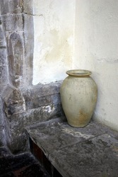 Earthenware Urn Standing On A Slate Plinth Against  A Wall Inside And Ancient Building