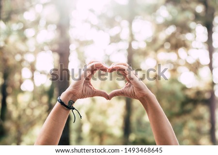 Earth's day concept with pair of human people hang doing hearth symbol with beautiful defocused forest in background - no fire and deforestation message for future generation and healthy planet