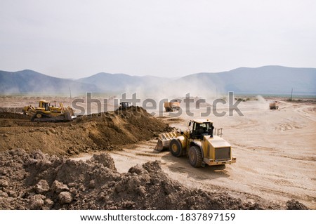 Earthworks in an open area on a summer sunny day. Cargo dump trucks, excavators, wheel loaders and bulldozers operate at the same time.