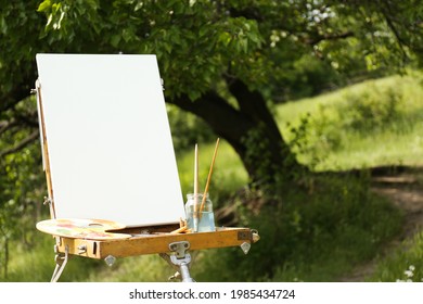 Easel with blank canvas and painting equipment in picturesque countryside - Powered by Shutterstock