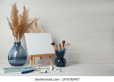 Easel with blank canvas, paints and brushes on white wooden table. Space for text - Powered by Shutterstock