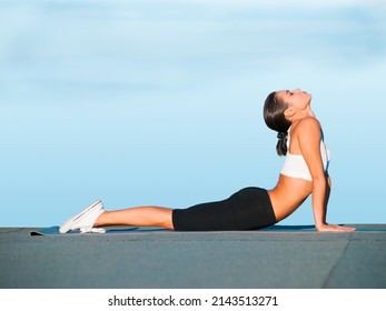 Easing Her Back Muscles Into A Stretch. A Young Woman Doing Yoga Outdoors Against A Blue Sky.