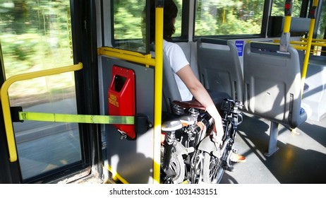 East Asian Woman Carries Folding Bicycles On A Public Bus. Folding Bikes Are Officially Allowed Being Carried On Public Bus In The UK.
