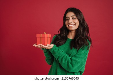 East asian woman smiling while posing with gift box isolated over red background