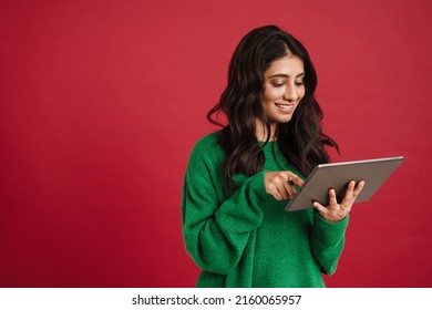 East Asian Woman Wearing Sweater Smiling While Using Tablet Computer Isolated Over Red Background