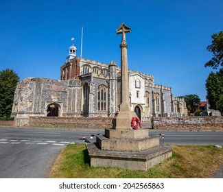 The East Bergholt Cross, Or War Memorial, With The Church Of St. Mary The Virgin In The Village Of East Bergholt In Suffolk, UK.