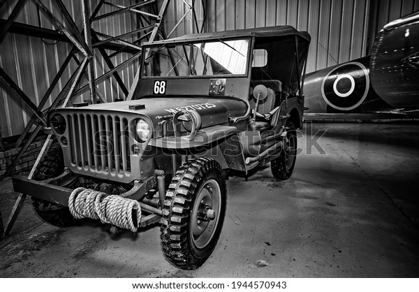East Fortune Museum of Flight, Scotland -\
August 2013: Black and white image of a World War 2 army jeep on\
display with plane in the\
background