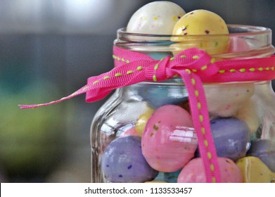 East Greenwich, RI/USA- April 5, 2015: A Horizontal Closeup Image Of Pastel Colored Candy Eggs Overflowing In A Glass Mason Jar Tied With A Pink Grosgrain Ribbon. 