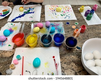 East Islip, NY, USA, March 28, 2021 Two Kids Paint Easter Eggs With Crayola Paint, Cups Of Dye, Paper Towels, Paint Brushes, And Creative Space. A Bowl With Unpainted Eggs Is Waiting To Be Decorated.