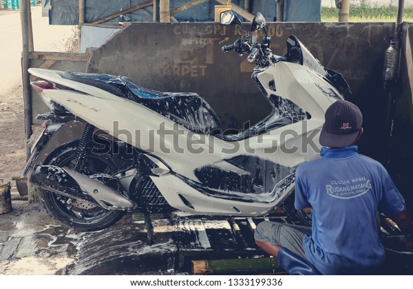 East Java, Indonesia -\
February 07, 2019 Local man washing HONDA PCX motorbikes on the\
side of the road