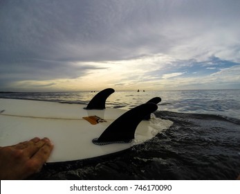 EAST JAVA, INDONESIA JANUARY 2017: Surfer Is Grasping Surfboard Upside Down While Waiting For The Next Set Of Waves (POV), With Other Surfers And Sunset In The Background