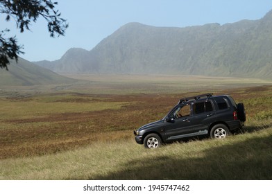 East Java, Indonesia - March 27 2021:The Old Metallic Black Suzuki Escudo 4WD Car Is Parked On A Stretch Of Savanna With A Hilly Background