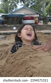 East Kalimantan, Indonesia - August 17, 2022 : A Little Girl Very Happy Playing On The Beach. Her Father Buried Part Of Her Body In The Sand So That She Laughed Out Loud