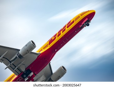 East Midlands Airport Leicestershire 3.5.2021 Yellow and Red DHL cargo aircraft jumbo jet taking off towards a blue sky with clouds blurring from motion. Wheels down after just lifting off runway.