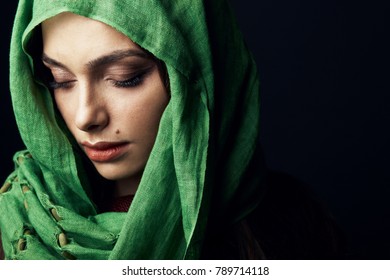 East style close-up studio portrait of attractive woman with big lips and birthmark near lips, wearing green hijab and looking down