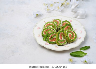 Easter appetizer, sliced spinach sponge roll with cream cheese and salted salmon on a light plate against a concrete background. Happy Easter. Spinach recipes