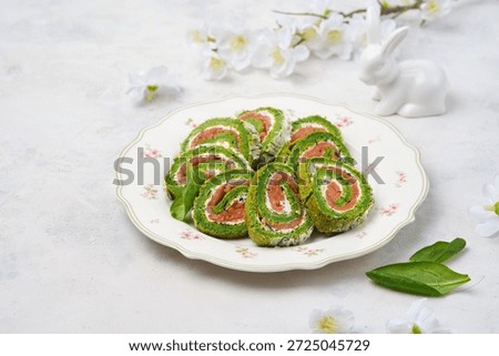 Easter appetizer, sliced spinach sponge roll with cream cheese and salted salmon on a light plate against a concrete background. Happy Easter. Spinach recipes