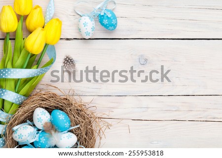 Easter background with blue and white eggs in nest and yellow tulips. Top view with copy space