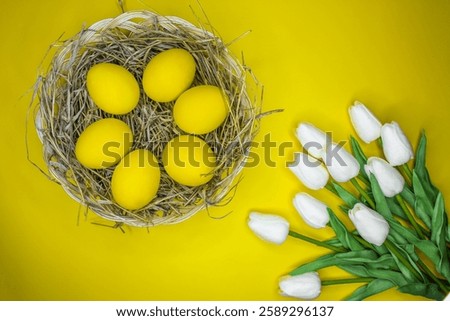 Easter background with bright yellow eggs and white tulips, top view. Easter composition. Top view of yellow Easter eggs on the yellow background.