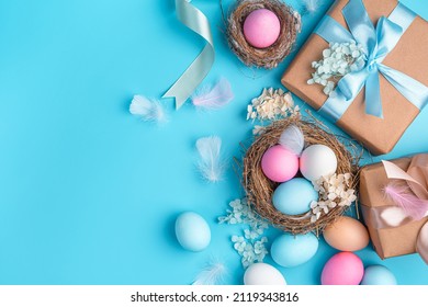 Easter background with colored eggs, nests and gifts on a blue background. Happy Easter. Top view, copy space.