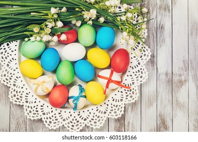 Easter background. Colored easter eggs and spring flowers on white wooden background.