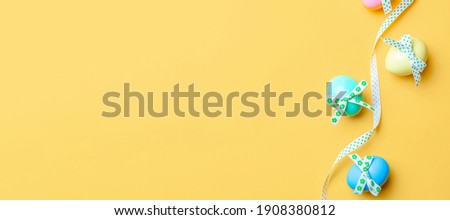 Easter background. Colorful egg with tape ribbon, spring tulips, feathers on pastel yellow background in Happy Easter decoration. Spring holiday top view banner