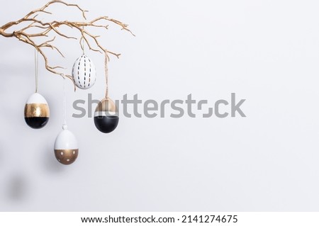 Easter background with copy space. Decorative golden, black and white Easter eggs hang on a golden branch and cast a shadow. Easter decorations.