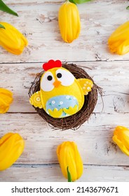 Easter Background With A Decorative Chick In A Nest Surrounded By Yellow Tulips On A Wooden Background. Vertical Photo