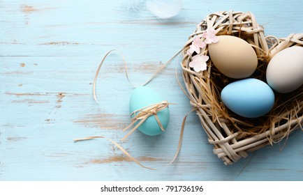 Easter background with Easter eggs in nest with shape of a heart on the blue wooden background . Top view with copy space.