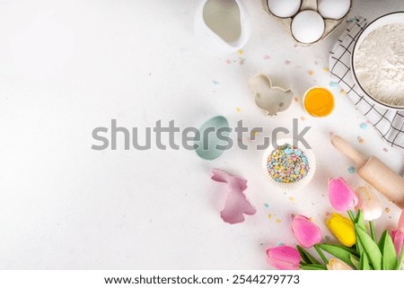 Easter baking background, ingredient for making Easter cookies, cakes, dessert with Easter chocolate eggs, sugar sprinkles, baking ingredients, flour, egg, milk, rolling pin, spring flowers top view