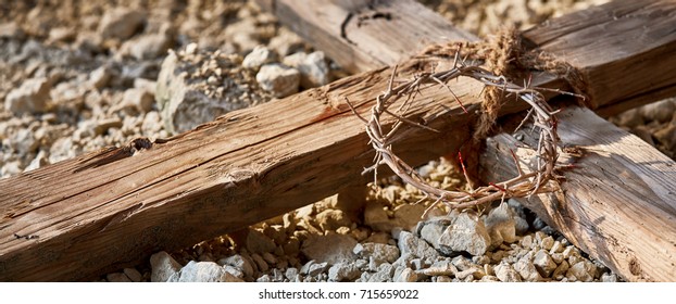 Easter banner commemorating the Crucifixion with a close up view of a wooden cross on stony ground with a bloodstained crown of thorns