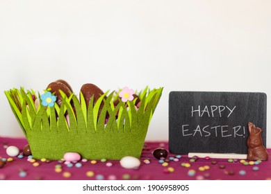 Easter Basket With Chocolate Eggs, Chocolate Bunny Missing A Bite And Blackboard With Happy Easter Text