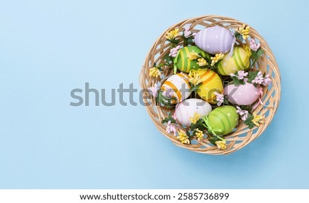 Easter basket with decorated colored eggs. Wicker basket with painted eggs and small flowers on a pastel blue background.