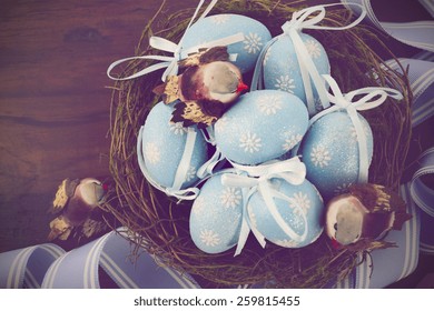 Easter blue decorative eggs in nest with robin birds and stripe ribbon on dark wood background, with applied retro vintage filters.