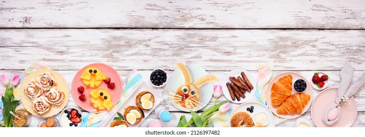 Easter breakfast or brunch bottom border. Top view on a white wood banner background. Bunny pancake, egg nests, chick fruit and an assortment of spring food items. Copy space.