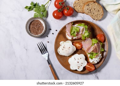 Easter breakfast or brunch. Delicious breakfast or snack - poached egg and cream cheese toast whole grain rye bread, prosciutto, arugula on a marble tabletop. Top view flat lay. Copy space. 