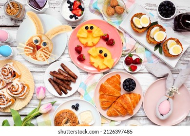 Easter breakfast or brunch table scene. Top view on a white wood background. Bunny pancake, egg nests, chick fruit and a collection of spring food items. Copy space.