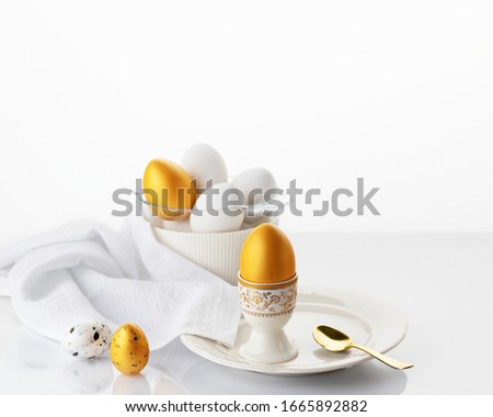 Easter breakfast concept. Soft boiled egg on a white plate with gold and white Easter eggs on a white background. Soft focus.