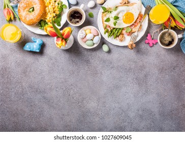 Easter breakfast flat lay with scrambled eggs bagels, orange tulips, bread toast with fried egg and green asparagus, colored quail eggs and spring holidays decorations. Top view. Copy space.