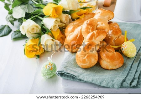 Easter breakfast Holliday concept. Easter bunny buns rolls with cinnamon made from yeast dough with orange glaze, easter decorations, colored eggs on white spring background. Easter Holliday card.