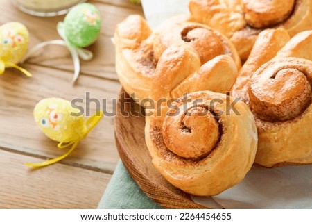 Easter breakfast Holliday concept. Easter bunny buns rolls with cinnamon made from yeast dough with orange glaze, easter decorations, colored eggs on old wooden background. Easter Holliday card.