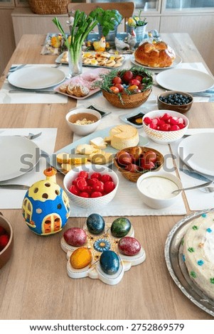 Easter breakfast table in natural light at home with plenty of food like ham, eggs, cheese, fruits, vegetables, cakes, cookies, ready for celebration in traditional way with plenty of decorations