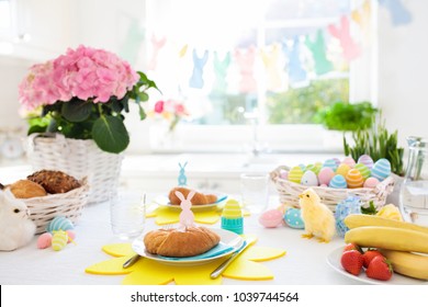 Easter Breakfast Table Setting. Decoration For Easter Family Celebration. Eggs Basket And Spring Flowers. Bread, Croissant And Fruit For Kids Meal. Egg And Pastel Bunny Decor In Kitchen At Window.